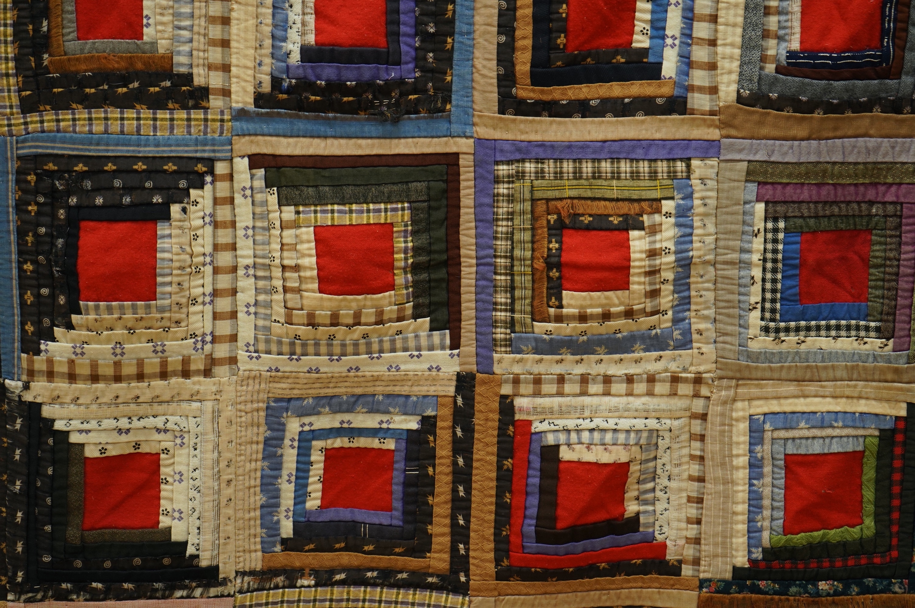 An early 20th century American ‘Log Cabin’ quilt, with a simple same coloured squared patchwork under side, the ‘Log Cabin’ worked in narrow bands of multi patterned and coloured strips of fabric into squares with a plai